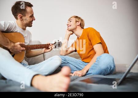 Fröhlicher junger Mann beobachten, wie Freund Gitarre spielen Stockfoto