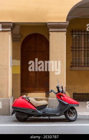 Ein roter Motorroller parkte vor einem Gebäude auf einem Straße in Bologna Italien Stockfoto