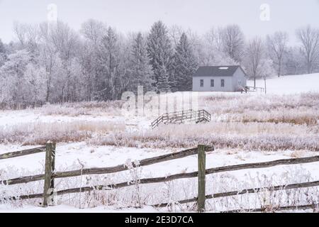 Neblige ländliche Winterlandschaft mit Scheune, Zaun und einer Brücke. Rime-Eis bedeckt die Bäume. Aufgenommen in Scandia, Minnesota Stockfoto