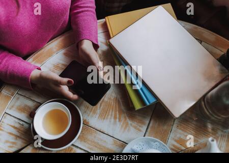 Draufsicht auf junge Frau, die am Tisch sitzt mit Tee und Tippen auf dem Smartphone im Café Stockfoto