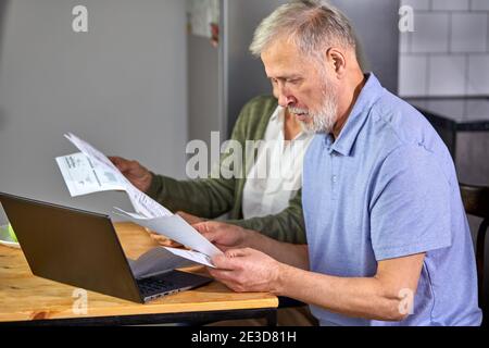 Senior paar Rechnungen überprüfen, während die Verwaltung von Konten auf Home-Banking-App. Casual grauhaarige Mann und Frau mit Laptop, während Blick auf Rechnung und p Stockfoto