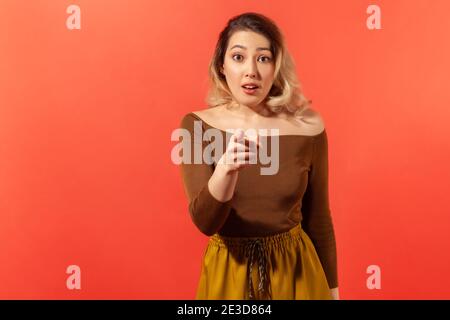 Das sind Sie! Porträt der wunderten Frau in braunen Bluse und gelbe Hose zeigt mit Finger auf die Kamera, Blick schockiert erstaunt mit offenem Mund, har Stockfoto