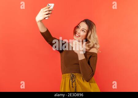 Positive schöne Frau macht Selfie oder Video-Aufnahme auf dem Smartphone für ihre Abonnenten, zeigt Daumen nach oben, fragen, wie ihre Beiträge. innenstudi Stockfoto