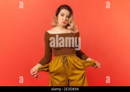 Schlechte Studenten, Arbeitslosigkeit. Porträt von verärgert arbeitslos Frau in braunen Bluse aus leeren Taschen, zeigt keine Geld Geste, besorgt über Schulden. Stockfoto