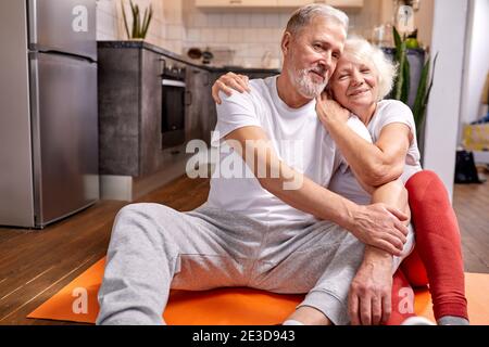 Ältere Paare, die sich nach Yoga-Übungen auf dem Boden ausruhen, in sportlicher Kleidung, in die Kamera schauen und lächeln Stockfoto