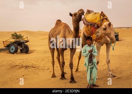 Junge Rajasthani Porträt und seine Kamele. Foto aufgenommen am 12. August 2018 in der Nähe von Jaisalmer, Thar Wüste, Rajasthan County, Indien. Stockfoto