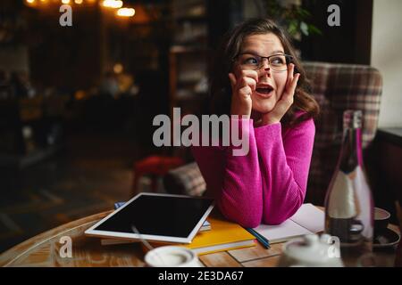 Lächelnde junge Frau, die mit Tablet arbeitet und gemütlich sitzt Cafe, während man Spaß hat Stockfoto