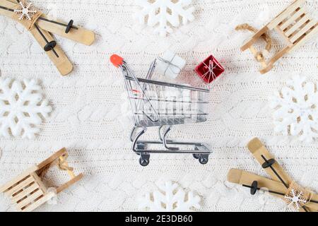 Winterflachlage mit Schneeflocken, Schlitten, Skiern, Geschenken und Warenkorb auf weißem gestricktem Hintergrund. Stockfoto