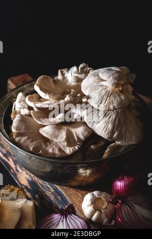 Austernpilze in einem alten Topf mit Gemüse auf dunklem Hintergrund. Nahaufnahme. Stockfoto