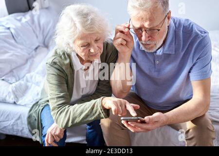 Senior paar Blick auf Kinderfotos in Smartphone, Online-Surfung Net, moderne Technologie-Konzept. kaukasische Frau und Mann mit Handy Sha Stockfoto