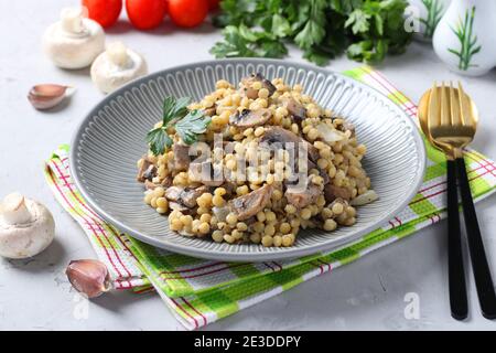 Hausgemachte Ptitim Pasta mit Champignons auf einem Teller auf hellgrauem Tisch. Horizontales Format. Stockfoto