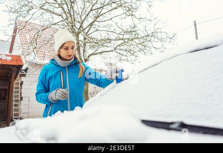 Frau kratzt Eis von der Frontscheibe ihres Autos Im Winter Stockfoto