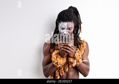 Schwarzer Mann in ethnischen Umhang schaut auf Smartphone, versuchen zu verwenden, Studium mit Interesse. Stockfoto