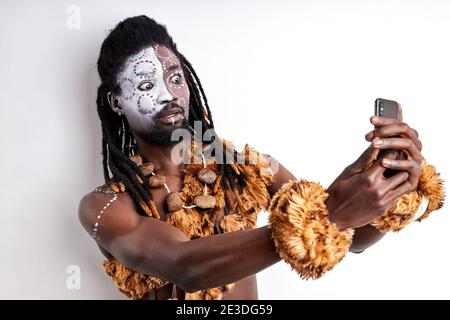 afrikanischer primitiver Mann mit Handy, er ist überrascht von modernen Technologien, stehen emotional reagieren auf Kamera, tragen ethnische nationale Kleidung Stockfoto