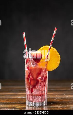 Rosafarbener Cocktail mit Eis und Erdbeeren, verziert mit Orangenscheibe Stockfoto