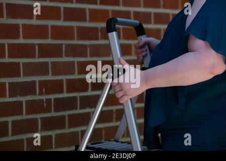 Frau, die eine Leiter in der Nähe eines roten Ziegels aufsetzt Wand Stockfoto