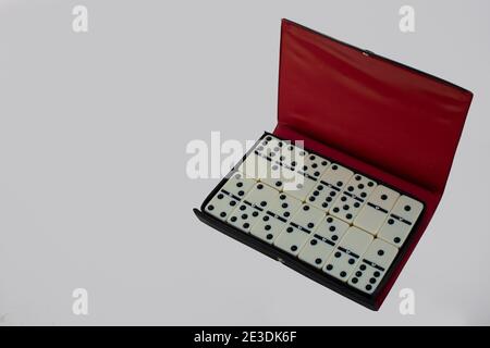 Domino-Set in einem offenen Gehäuse auf weißem Hintergrund isoliert angeordnet. Draufsicht mit leerem Platz für Text. Schwarzes und rotes Etui mit Domino Stockfoto