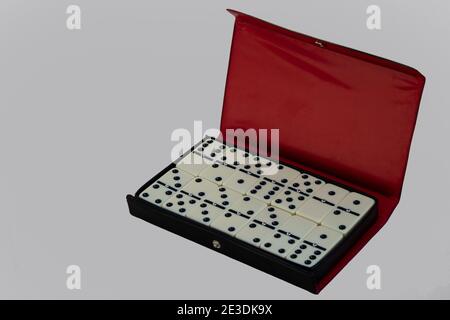 Domino-Set in einem offenen Gehäuse auf weißem Hintergrund mit leerem Platz für Text isoliert angeordnet. Schwarzes und rotes Etui mit Domino Stockfoto