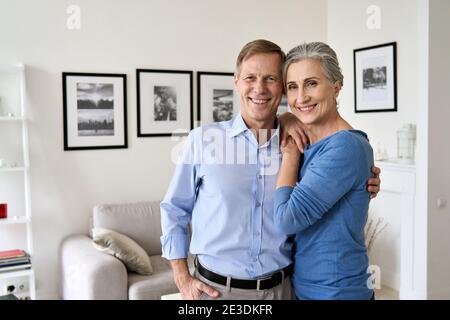 Glückliches älteres Paar umarmt, Blick auf die Kamera, sitzen auf der Couch in der Wohnung. Stockfoto