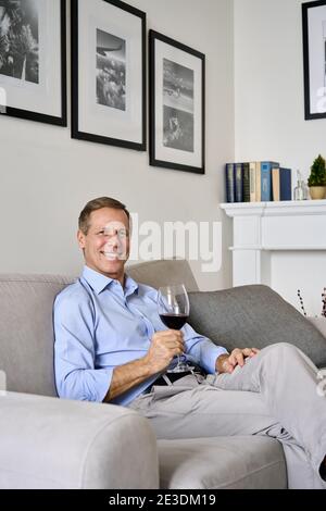Glücklich heiter reichen alten Senior Single Mann trinken Wein entspannen auf dem Sofa zu Hause. Stockfoto