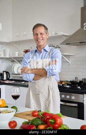 Glücklicher Mann mittleren Alters trägt Schürze Kochen Salat zu Hause, Porträt. Stockfoto