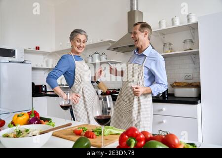 Glückliches Seniorenpaar, das zu Hause gemeinsam tanzt und gesundes Essen kocht. Stockfoto