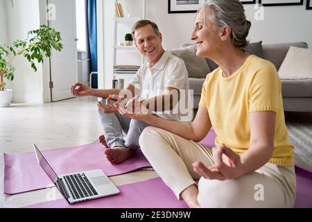 Glückliches Seniorenpaar, das Spaß hat, meditieren zu lernen, sich Online-Yoga-Kurs anzusehen. Stockfoto