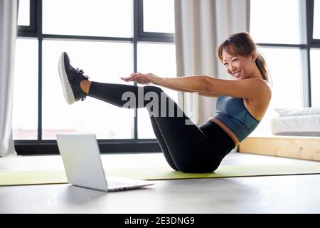 asiatische Frau Bewegung zu Hause, beobachten Video-Tutorial auf Laptop, Training auf dem Boden. Sport Online-Konzept Stockfoto