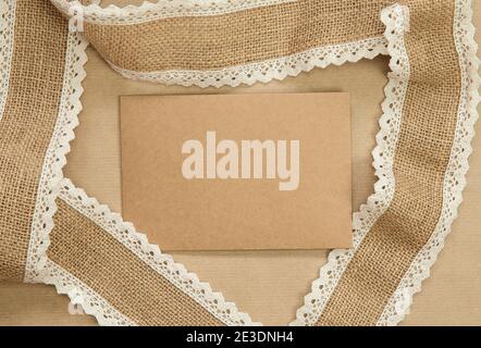 Flach Lay Komposition mit blank braun einfarbig Grußkarte mit natürlichen Quappe Band auf Bastelpapier Hintergrundtextur umgeben, Draufsicht Design Stockfoto