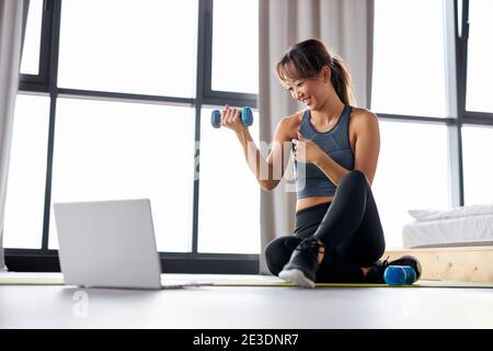 asiatische Frau Bewegung zu Hause, beobachten Video-Tutorial auf Laptop, Training mit Hanteln auf dem Boden. Sport Online-Konzept Stockfoto