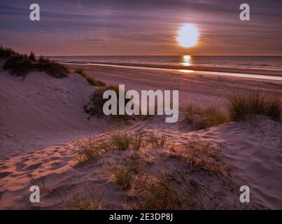 Blick von Marram Gras bedeckten Dünen in Richtung Strand vor Zu einem bunten Sonnenuntergang Stockfoto