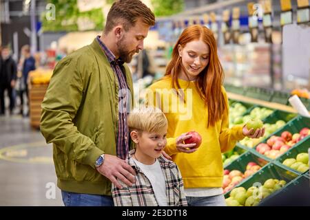 Familie mit Kind Junge im Lebensmittelgeschäft, kaukasischen Eltern und Kind kaufen frische Früchte Äpfel, diskutieren Stockfoto