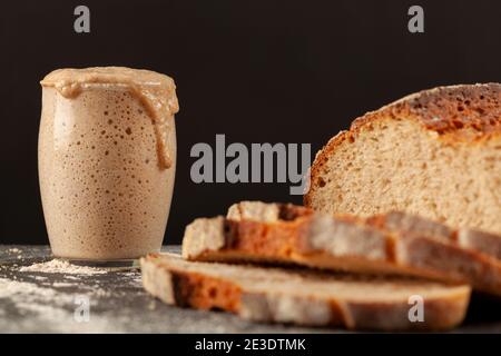 Nahaufnahme Seitenansicht eines frisch gebackenen Sauerteigs mit dickem Kruste, handwerkliches Brot mit einer aktiven Sauerteig-Starterkultur im Hintergrund. Ris Stockfoto