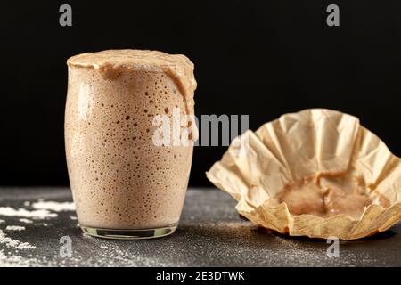 Seitenansicht einer aktiv ansteigenden Sauerteig-Starterkultur, die über die Oberseite des Glasbechers überläuft, in dem sie sich befindet. Bläschen zeigen Gärung. Der Stockfoto