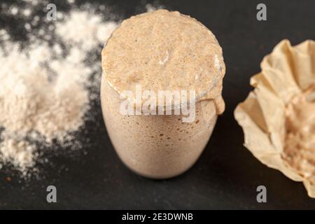 Draufsicht auf eine aktiv ansteigende Sauerteig-Starterkultur, die über die Oberseite des Glasbechers überfließt, in dem sie sich befindet. Bläschen zeigen Gärung. Das c Stockfoto