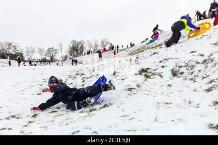 Kind Kind fällt beim Rodeln auf dem Gelände des antiken Amphitheaters im Winter auf Becsi-Domb, Sopron, Ungarn Stockfoto