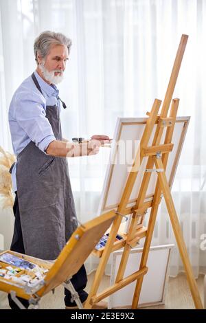 Künstler in die Schaffung von Kunst eingetaucht, Malerei Leinwand auf Staffelei. Handwerker in Schürze genießen Malerei Stockfoto