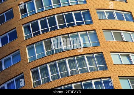 Fassade eines hohen modernen mehrstöckigen Gebäudes, einem Wolkenkratzer. Hintergrund eines gelben Wohnturms, große Glasfenster, Stadtarchitektur. Stockfoto