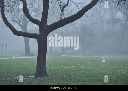 Blick auf den Vondelpark im Winternebel. Ein kleiner, schmelzender Schneemann ist auf der rechten Seite des Bildes, zwischen den kahlen Bäumen. Stockfoto