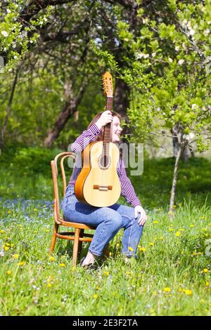 Blonde attraktive Teenager-Mädchen mit der Gitarre im Frühling Garten. Stockfoto