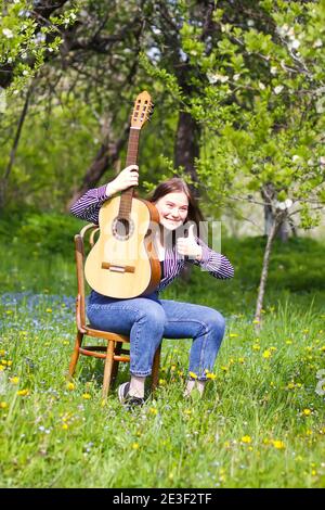 Blonde attraktive Teenager-Mädchen mit der Gitarre im Frühling Garten. Stockfoto