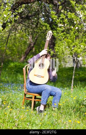 Blonde attraktive Teenager-Mädchen mit der Gitarre im Frühling Garten. Stockfoto