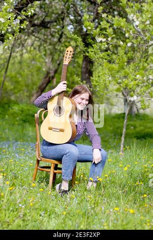 Blonde attraktive glücklich Teenager Mädchen mit der Gitarre im Frühling Garten. Stockfoto