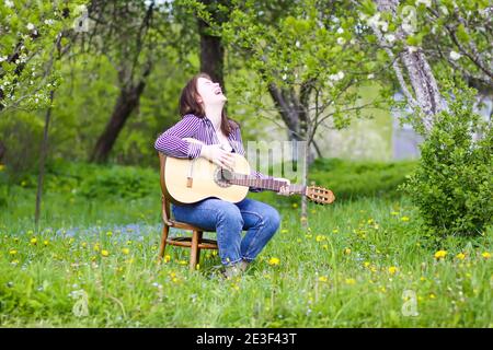 Blonde attraktive Teenager Mädchen Gitarre spielen im Frühling Garten. Stockfoto