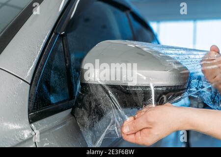 Arbeiter Hände wickelt nasse Lackschutzfolie oder Anti-Kies-Schutz-Beschichtung auf Autospiegel. Details zum Fahrzeug. Stockfoto