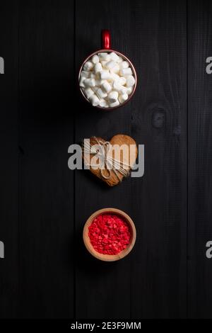 Rote Tasse Kaffee mit Marshmallows, herzförmigen Lebkuchen und Gebäck Belag auf schwarzem Holz Hintergrund. Draufsicht Stockfoto