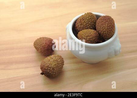 Bild von einigen Litchis (Litchi chinensis) In einer Schüssel, die auf einem Holztisch steht Stockfoto