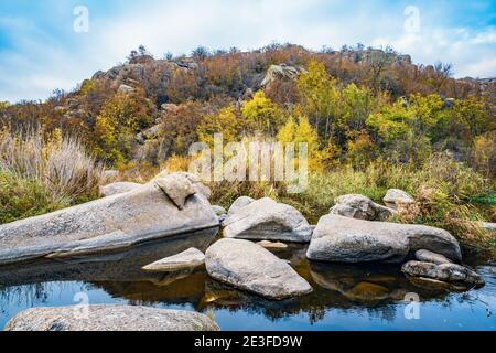 Ein schneller, flacher, sauberer Bach fließt zwischen glatten nassen großen Steinen, umgeben von hohen trockenen Klumpen, die im Wind im malerischen Ukraine schwanken Stockfoto