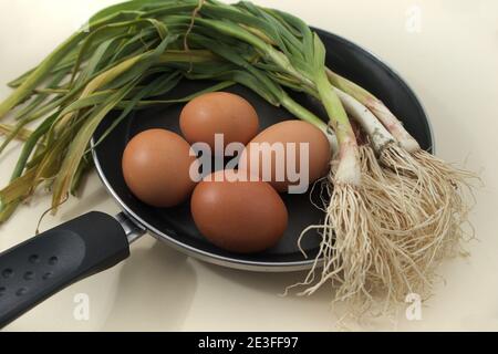 Flache Lage einer Pfanne mit jungen Knoblauch und braun Eier für die Herstellung eines Knoblauch Omelette zu Hause Stockfoto
