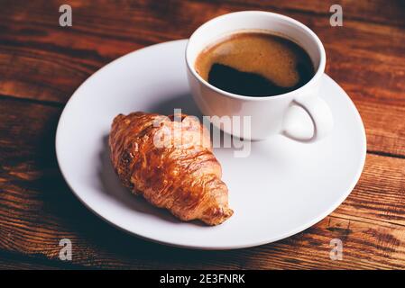 Tasse schwarzen Kaffee und frischen Croissant auf weißem Teller Stockfoto